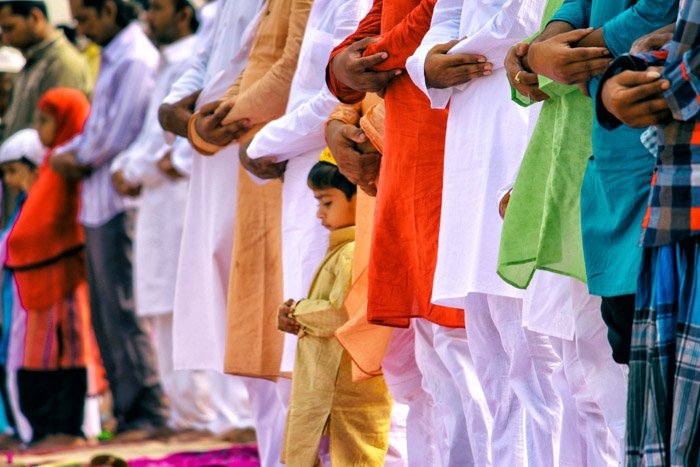 A crowd of people with arms folded in prayer, focused on a little boy