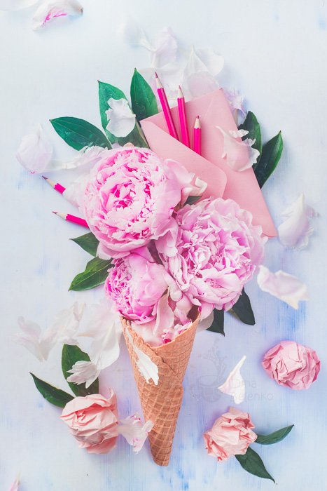 A bright and airy flat lay still life with an ice-cream cone filled with roses on a light background