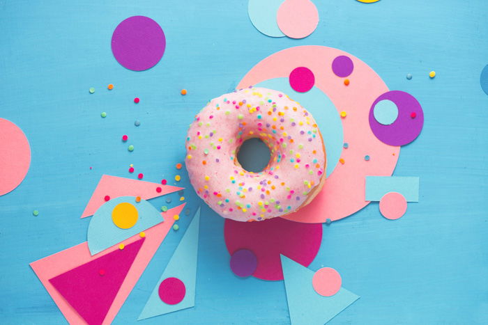 quirky flat lay of a pink doughnut on blue surface surrounded with pink paper