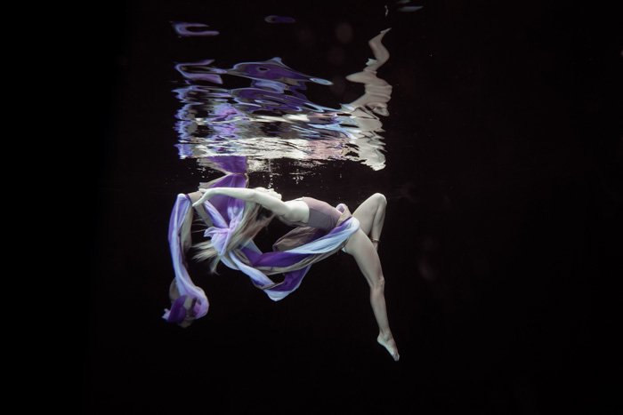 Stunning underwater photography shot of a girl posing with purple and while fabric while swimming underwater