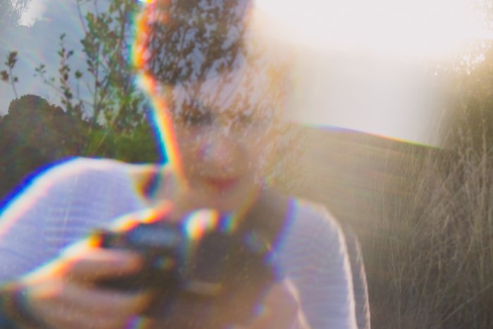 A woman in a stripy top holding a camera, overlayed with dreamy prism photo effect
