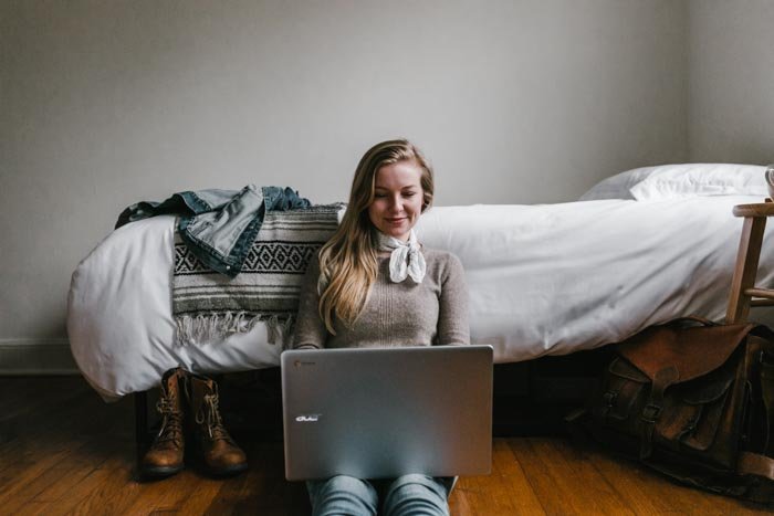 A girl sitting on a bedroom floor editing photos on a laptop