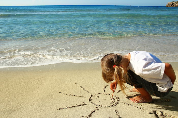 A child drawing a sun in sand on a beach by the ocean