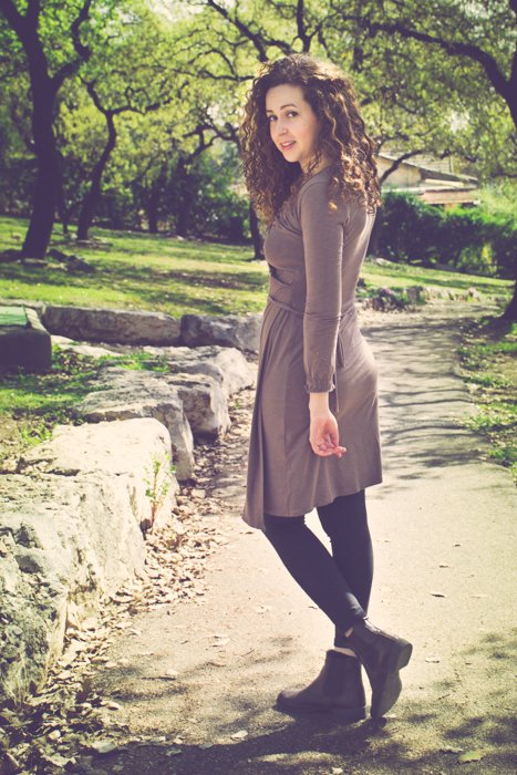 curly haired brunette in a brown dress and boots looking back while walking down a dirt path in a park - cropping photos