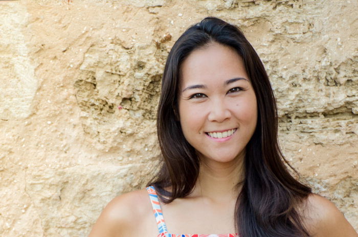 photo cropped below shoulders of smiling asian woman in front of a sandy stone wall