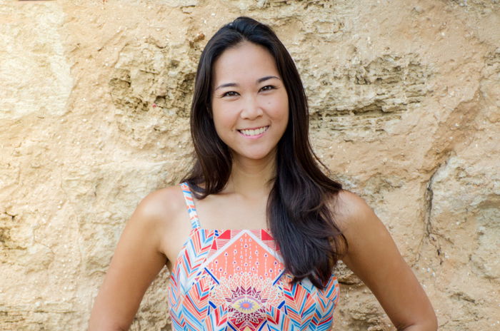 photo cropped at elbows of smiling asian woman in a pastel geometric patterned dress standing in front of a stone wall 