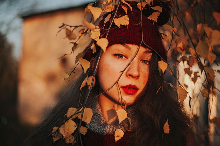 Beautiful close up portrait of a girl outdoors with tree branches in front of her face, shot using ambient lighting for a dreamy effect