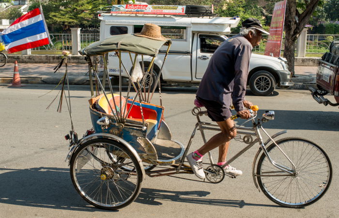 A documentary photography shot of a samlar driver rising down the street