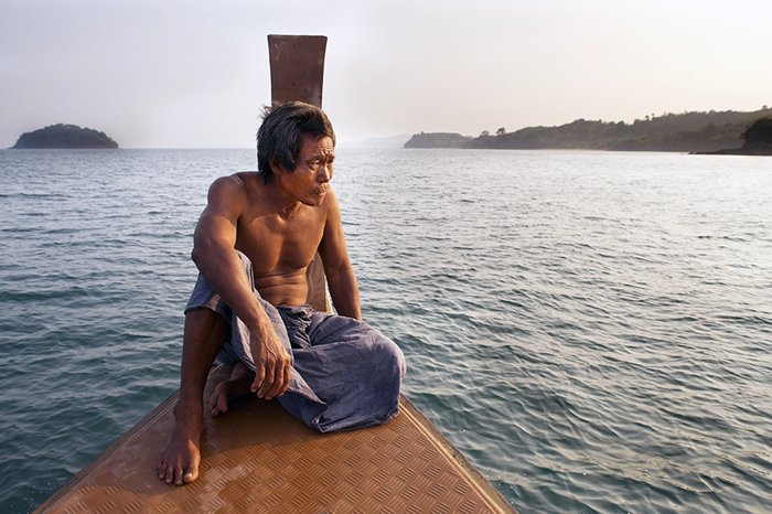 A man sitting on a small wooden boat at sea
