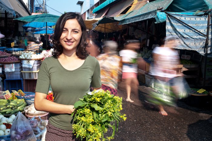 Young woman standing in a busy market. Shot using a slow shutter speed to get the movement of the people blurred.