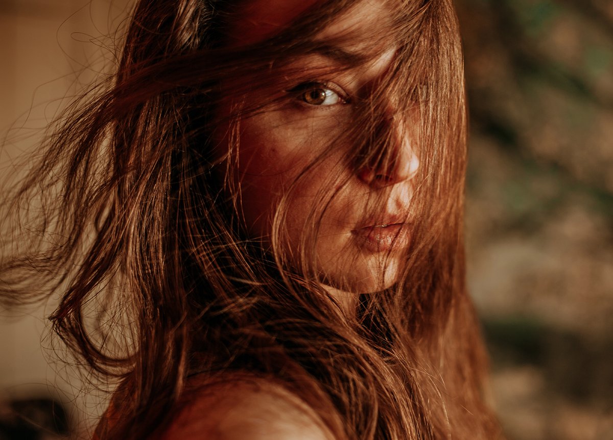 A close-up portrait of a woman with hair across her face taken with ambient light