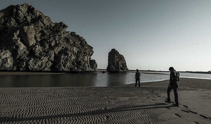 A black and white fine art photography shot of a rocky beach, with a soft misty effect of the water around the rocks and cliffs