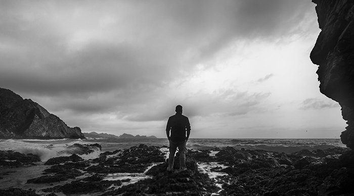 A black and white fine art shot of a man on a beach looking towards the ocean