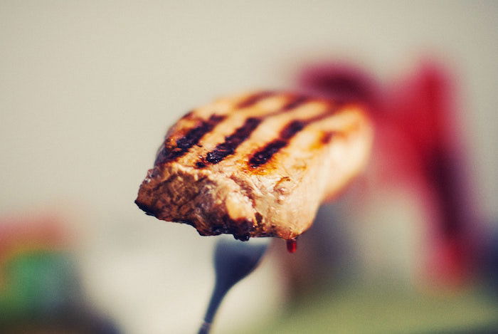 A close up photo of a piece of barbequed meat on a fork with bokeh background