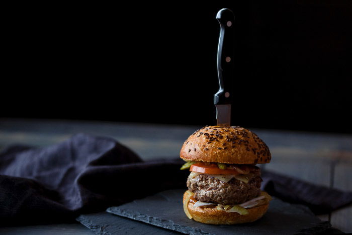 Dark and moody food styling example of a burger with a steakknife through it, against a dark background