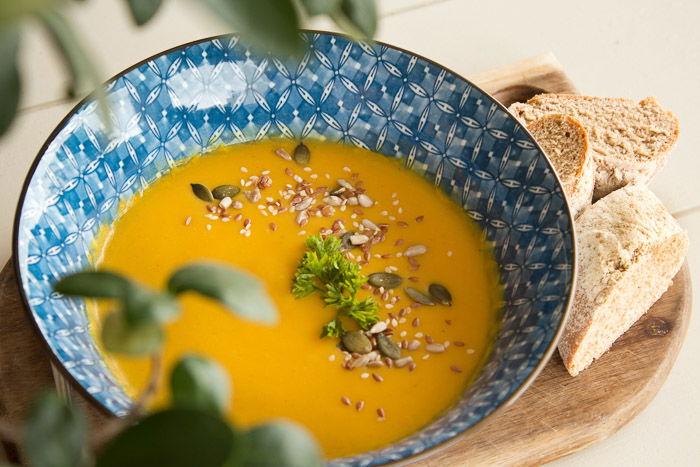 Overhead shot of orange soup in abowl, with bread and leaves beside it