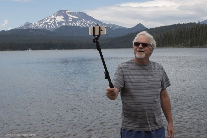 A man taking iphone photo of himself with a selfie stick