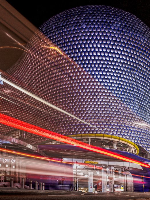The Bullring Shop Center in Birmingham with the light trails from a double decker bus passing in front 