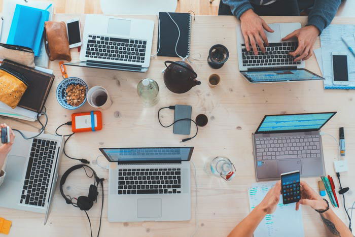 Overhead shot of 5 laptops on a messy office desk