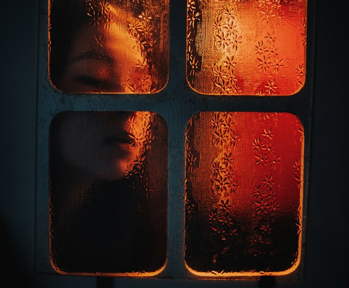 Atmospheric portrait of a girl with face pressed against a window pane with ambient lighting