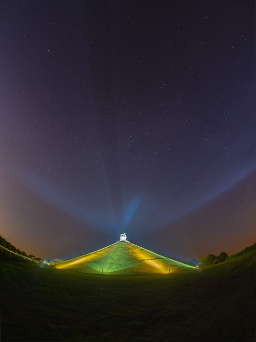 photo of La Butte Du Lion, Waterloo in Belgium, brightly lit in green and yellow, under the dark sky littered with stars.