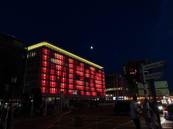 Photo of a rectangular building with lots of windows at night, with changing lights on its face