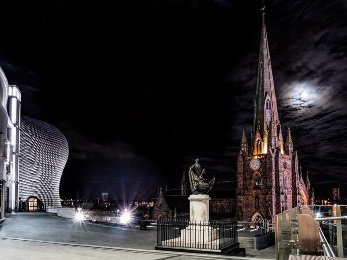 St Martin in Bullring, with the Nelson statue and the Bullring shop centre in Birmingham. The structure lit against a dark sky, the moon eerie behind clouds