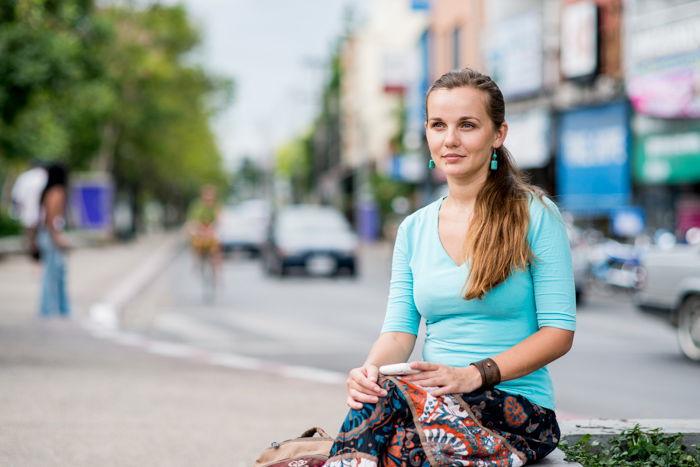 A smiling girl sitting on a wall with a blurred cityscape behind her during a photo shoot