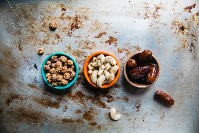 An overhead shot of three small bowls of nuts and dried fruit on a metal surface