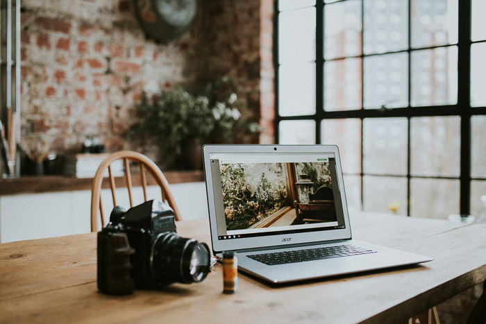 A laptop, film and camera set up on a wooden desk to prepare a photography business plan