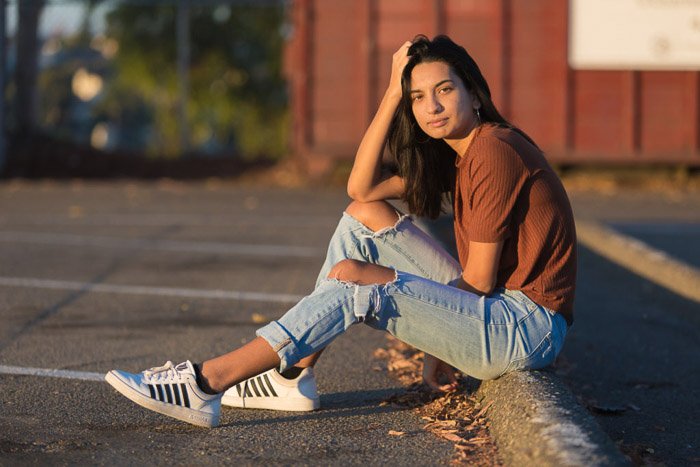 A photography business portrait of a young girl sitting down on a curb 