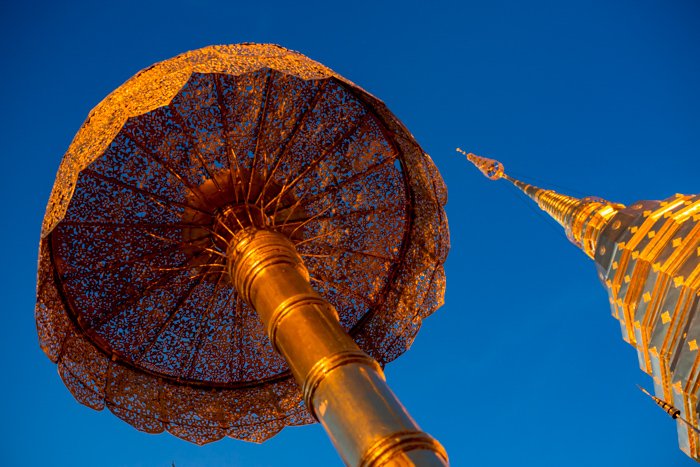 photo looking up at the Golden stupa and umbrella in buddhist temple in Chiang Mai, Thailand against a deep blue sky