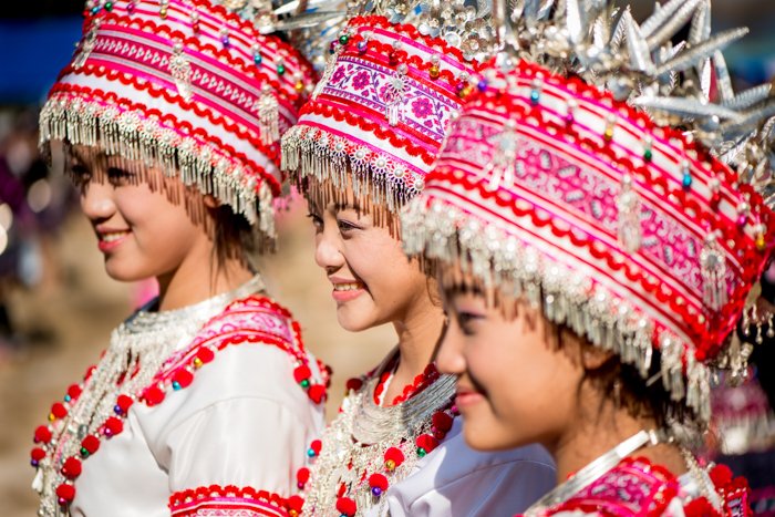 三个面带微笑的女孩，头戴红白相间的传统头饰，身穿传统服装