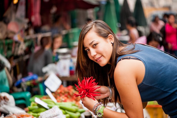 在一个新鲜的市场里，一个身穿无袖海军蓝衬衫的黑发女人微笑着俯身看着商品