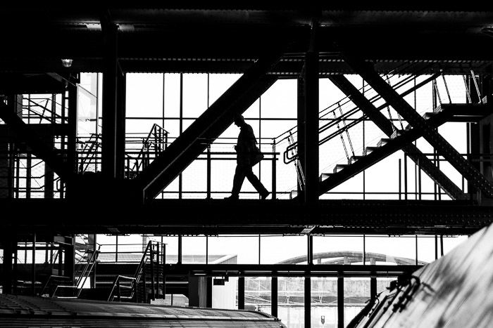 Black and white street photo of a man's silhouette against some windows.