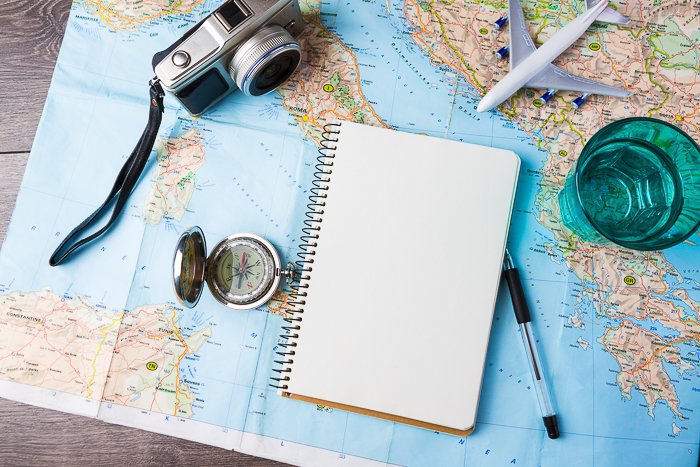 An overhead shot of a camera, notebook,pen and model plane on top of a map of the world 