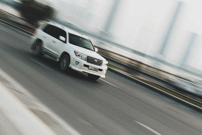 A white car driving, the background is a creative blur demonstrating shutter speed and its uses