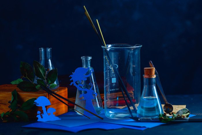A still life featuring glass bottles ,silhouettes of tiny cut out character, incense 