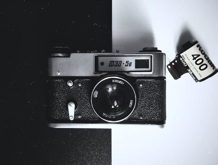 Una fotografía cenital de una vieja cámara de cine sobre fondo blanco y negro con un rollo de película al lado - usando película para fotografía callejera 