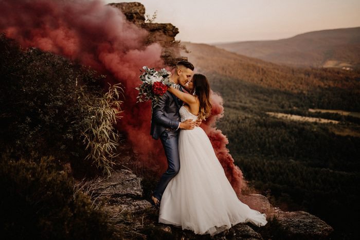 A newlywed couple embracing in an atmospheric landscape with smoke behind them from best wedding blog, junebug weddings