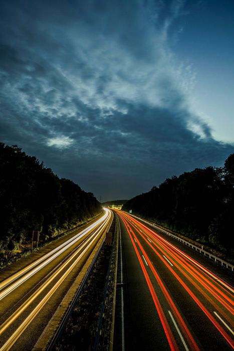 An aerial view of a highway at night with colored streams of light trails from cars 