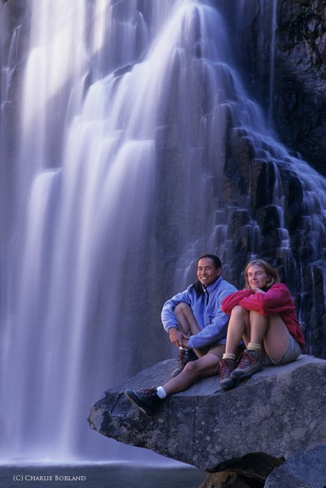 two campers sitting on a rock in front of a waterfall