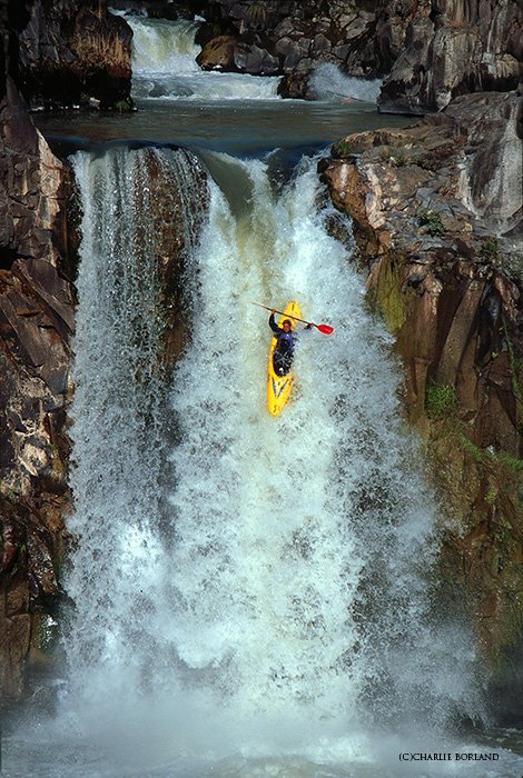 man rowing the rapids in a yellow canoe going down a waterfall