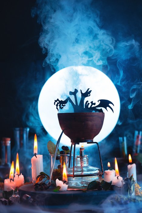 Atmospheric Halloween still life featuring a a cauldron, a full moon, candles and other spooky props