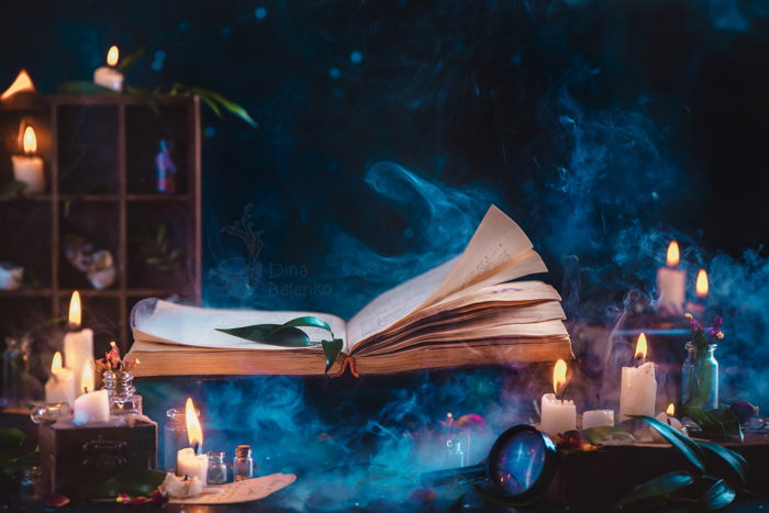 A spooky Halloween photography still life featuring a spellbook, candles and other photography props 