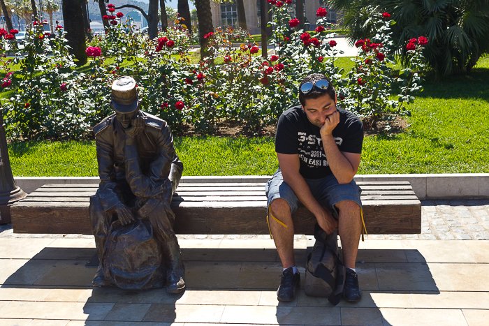 A man sitting beside a statue on a bench 