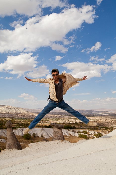jumpshot of a man in jeans and sunglasses, on a dust road overlooking rocky cliffs on a bright sunny afternoon