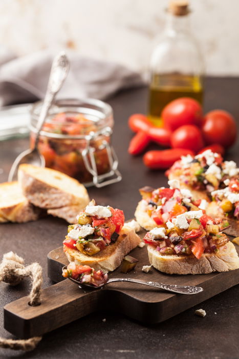 aperitivo de bruschetta servido en una bandeja de madera, con tomates y un tarro de aceite de oliva cerca
