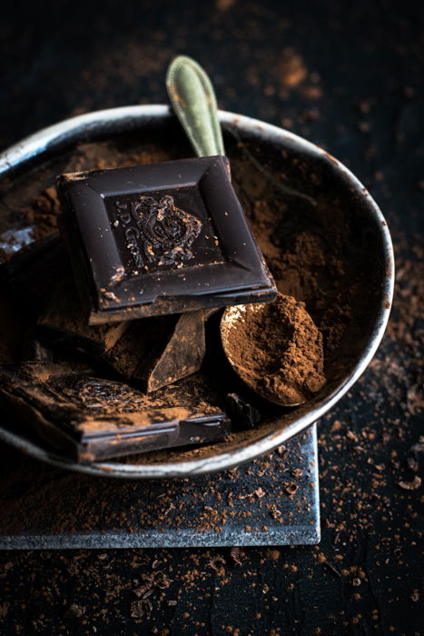 De cerca un cuenco de trozos de chocolate negro y una cuchara cubierta con chocolate en polvo