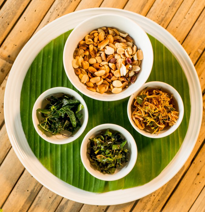 A centrally placed round plate with four round bowls and the green banana leaf 